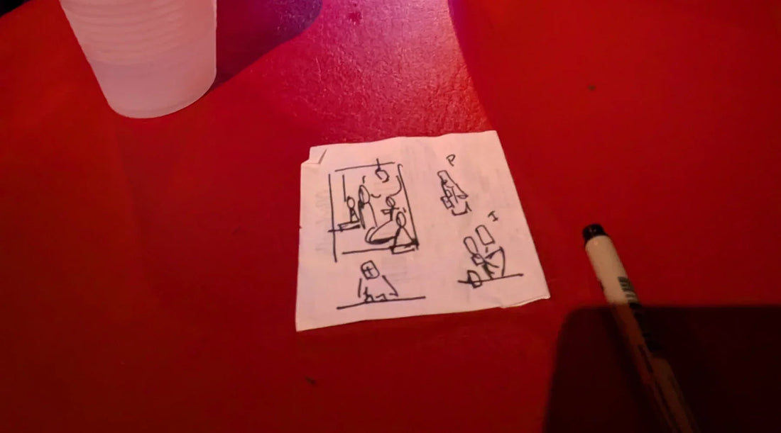 A scrap of receipt paper sits on a red table at a bar in downtown Houston.  The paper has some small drawings on them that will be used for a painting.